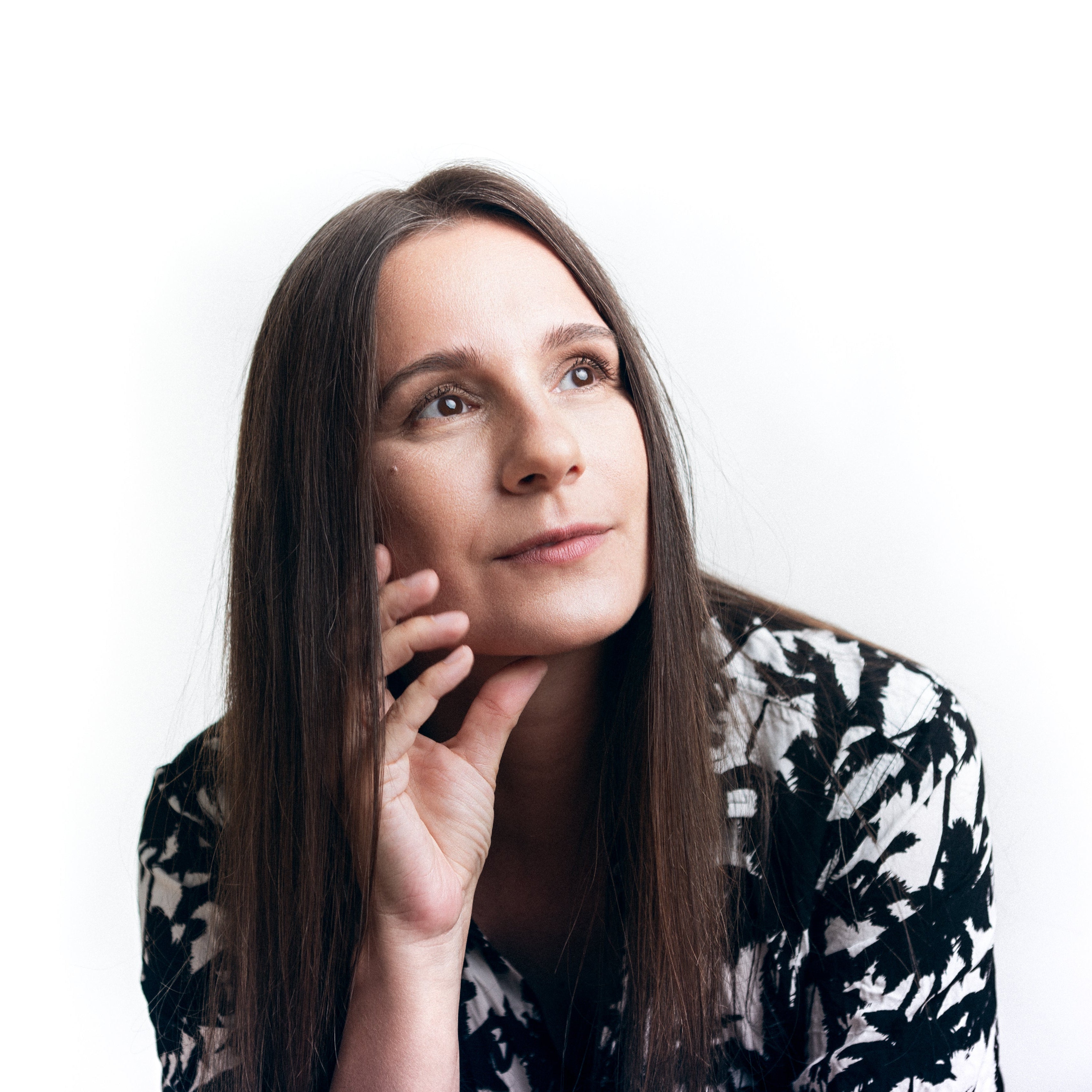Dana Ruh with long brown hair wearing a black and white patterned top against a white background - Presskit Picture